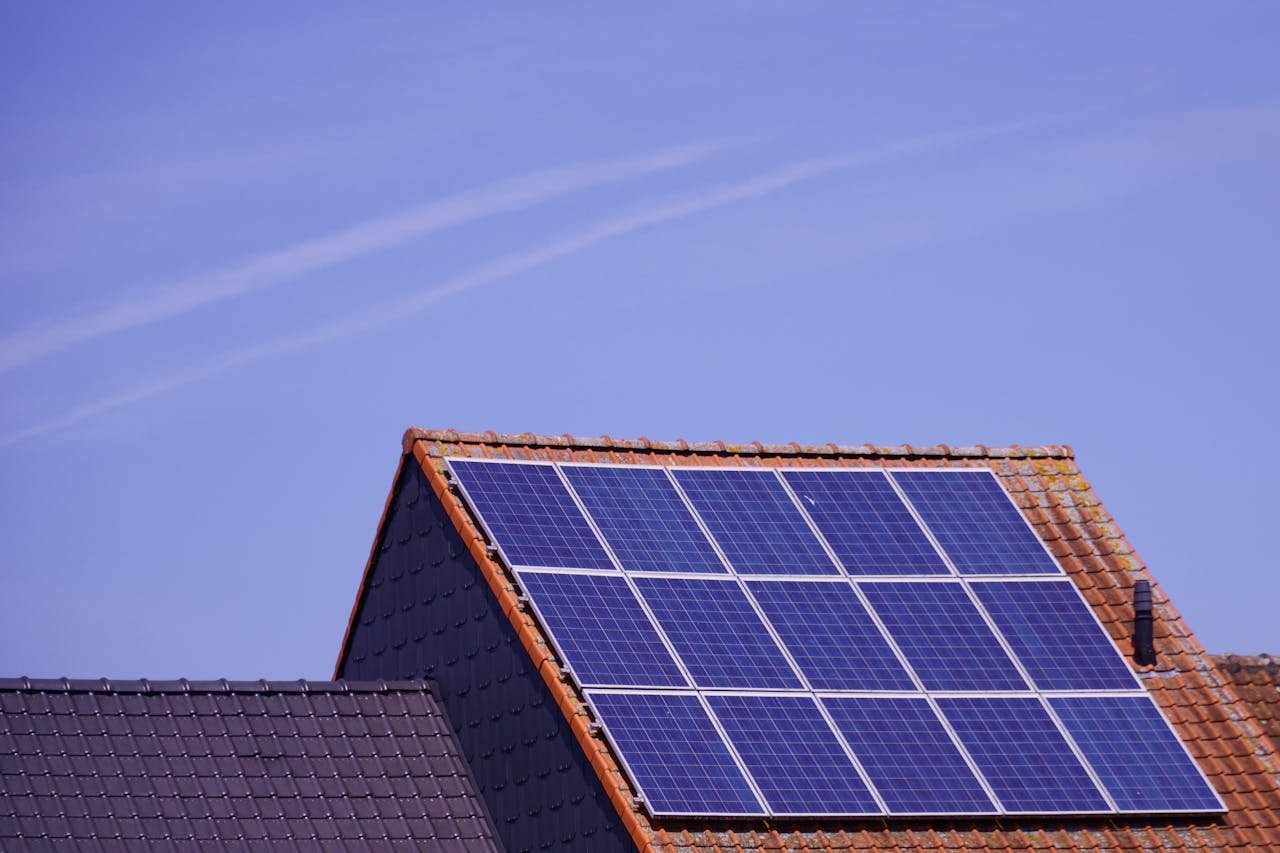 Saulės elektrinės ant namo stogo saulėtą dieną, demonstruojančios efektyvų namų energijos naudojimą.