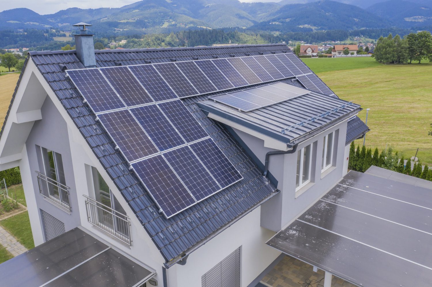Saulės elektrinė ant gyvenamojo namo stogo saulėtą dieną, rodanti švarios energijos gamybą.